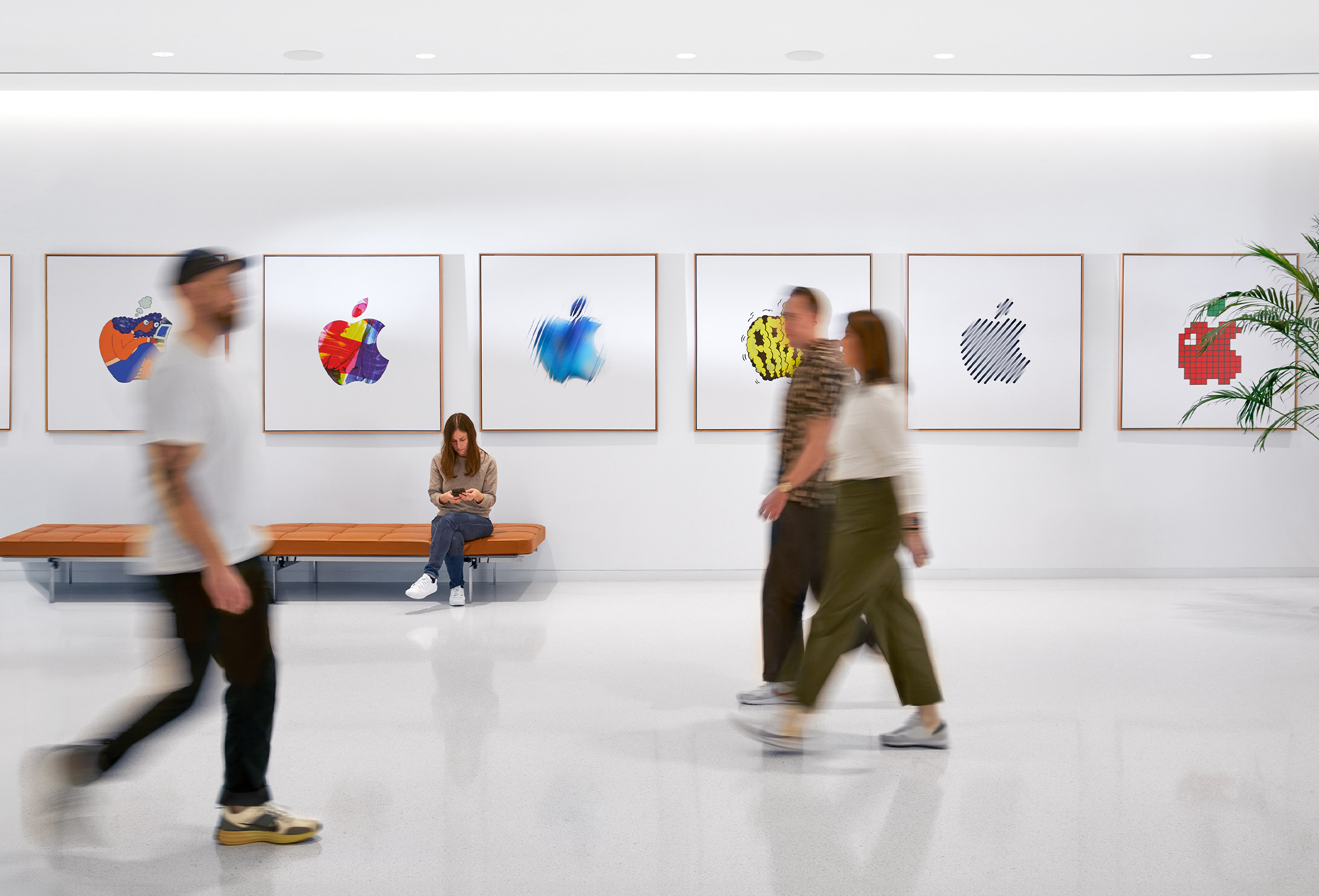 Drie Apple medewerkers wandelen langs een wand met kleurrijke Apple logo’s. Een vierde medewerker zit op een bank.