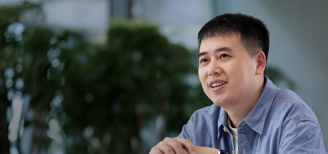 Ken นั่งอยู่ในอาคารที่ตกแต่งด้วยต้นไม้