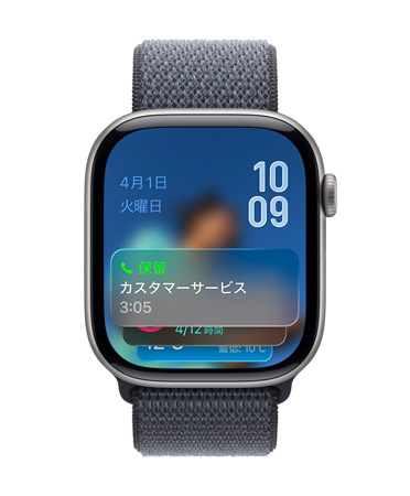 グレイのバンドを組み合わせたスペースグレイのApple Watch。画面の下部に保留アシスタントの通知、左上に日付、右上に上下に重なった時刻が表示されている