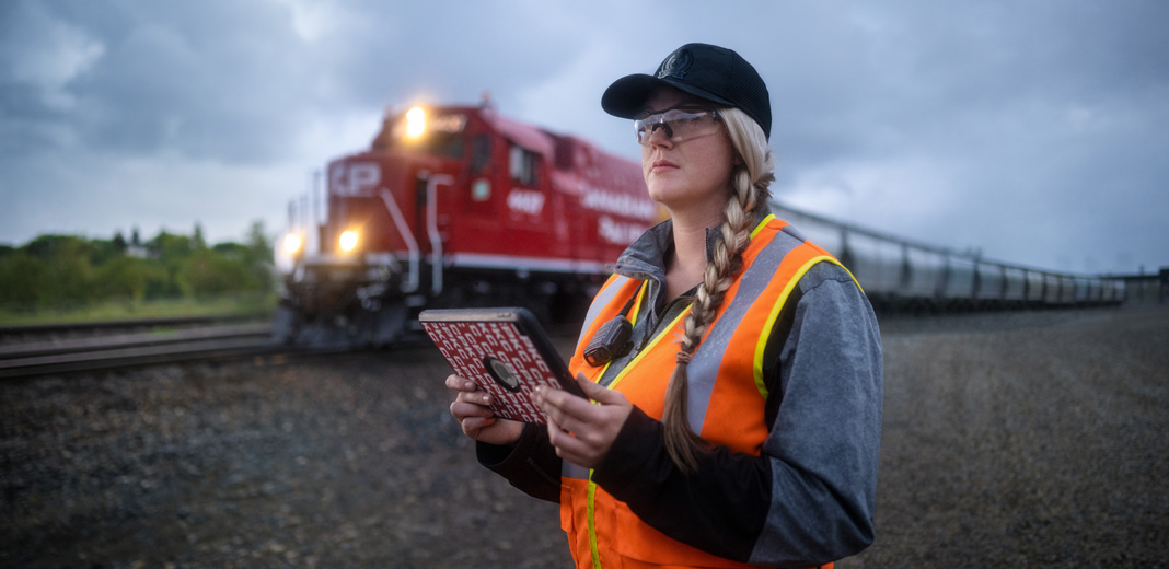 Une employée des chemins de fer regarde les voies en tenant un iPad pendant qu’un train passe