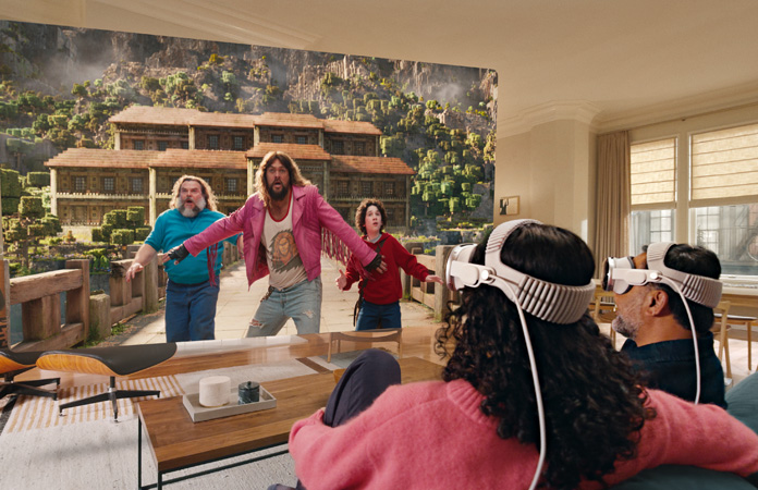 Deux personnes portant un Apple Vision Pro assises côte à côte sur un canapé regardent le film Fountain of Youth sur un écran qui s’étend d’un bout à l’autre de la pièce